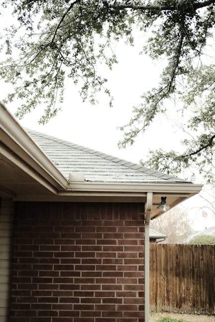A serene view of a red brick house corner with overhanging tree branches. Residential Gutter Cleaning Services in Alabama A serene view of a red brick house corner with overhanging tree branches.